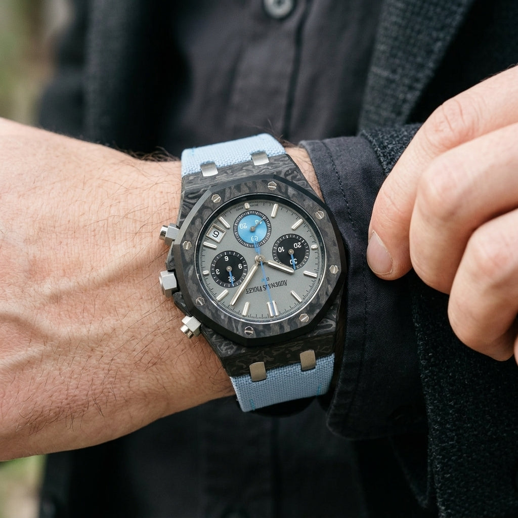 Black forged-carbon octagonal chronograph with a grey dial and a sky-blue counter on the wrist as a shirt cuff is fastened