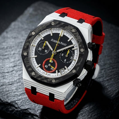 White octagonal chronograph at a three-quarter angle on dark slate, thin black lines along its flank beside the black crown and pushers