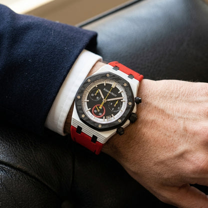 White octagonal chronograph with a black carbon bezel on its red canvas strap, worn on the wrist below a dark suit cuff