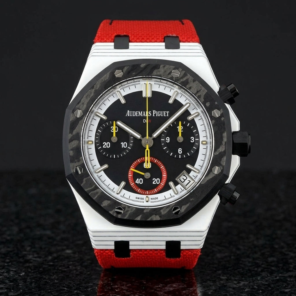 White octagonal chronograph with a black carbon bezel on its red canvas strap, worn on the wrist below a dark suit cuff