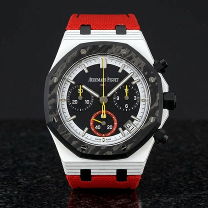 White octagonal chronograph with a black carbon bezel on its red canvas strap, worn on the wrist below a dark suit cuff