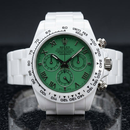 White ceramic chronograph with a green Roman numeral dial and a white tachymeter bezel, upright on polished black granite