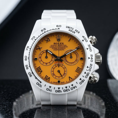 White ceramic chronograph with a mango-orange dial and black Roman numerals, upright on polished black granite