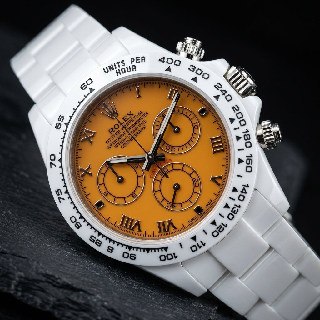 White ceramic chronograph at a three-quarter angle on dark slate, the polished steel crown and pushers beside the white tachymeter bezel