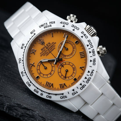 White ceramic chronograph at a three-quarter angle on dark slate, the polished steel crown and pushers beside the white tachymeter bezel