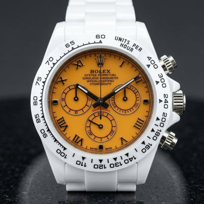White ceramic chronograph with an orange dial on its white ceramic bracelet, worn on the wrist below a dark suit cuff