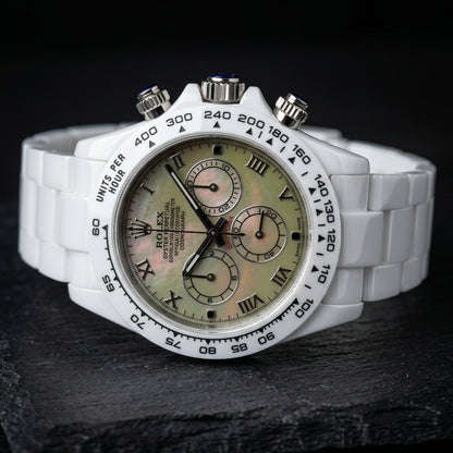 White ceramic chronograph at a three-quarter angle, the steel crown and pushers capped with deep-blue stones