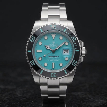 Steel dive watch with a turquoise dial and a black ceramic bezel, upright on polished black granite