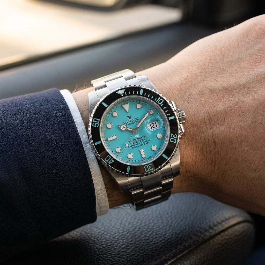 Steel dive watch with a turquoise dial on its three-link bracelet, worn on the wrist below a navy suit cuff
