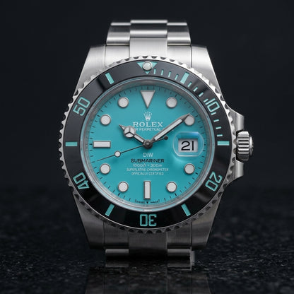 Steel dive watch with a turquoise dial on its three-link bracelet, worn on the wrist below a navy suit cuff