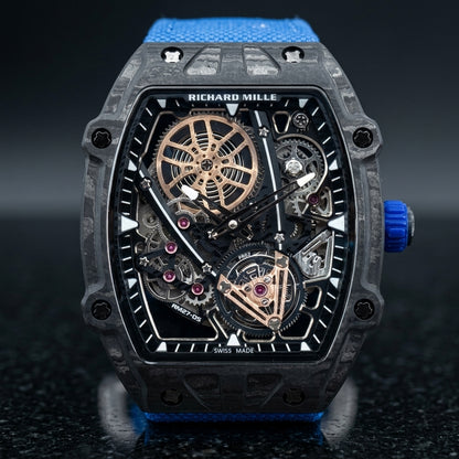 Black carbon flying tourbillon watch on a blue woven strap, worn on the wrist below a navy suit cuff