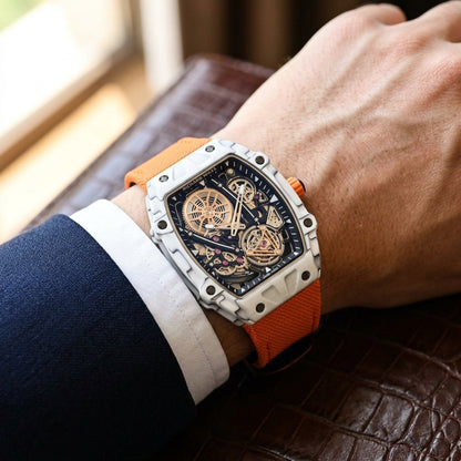 White carbon skeleton tourbillon watch on an orange woven strap, worn on the wrist below a navy suit cuff