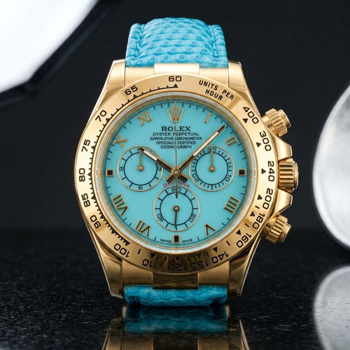 Gold-tone chronograph with a turquoise dial, gold Roman numerals and an engraved tachymeter bezel standing upright on polished black granite