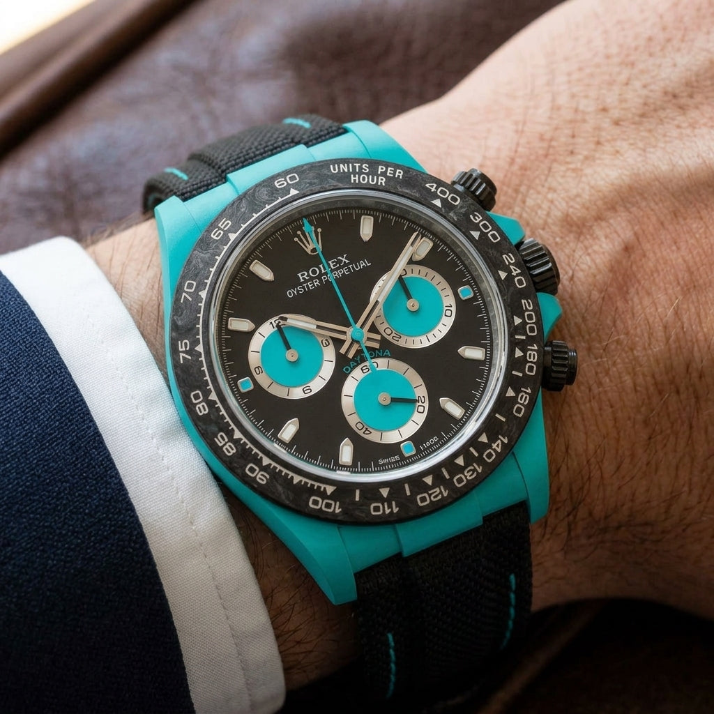 Turquoise-cased chronograph on a black woven strap with turquoise stitching, worn under a cuff