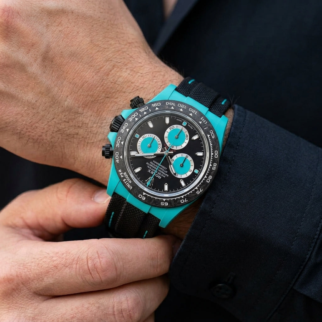 Turquoise-cased chronograph with a forged-carbon bezel and a black dial on the wrist as a shirt cuff is fastened
