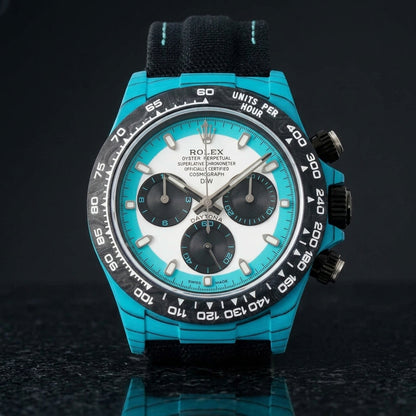Turquoise-cased chronograph with a black carbon bezel and white dial on pale stone