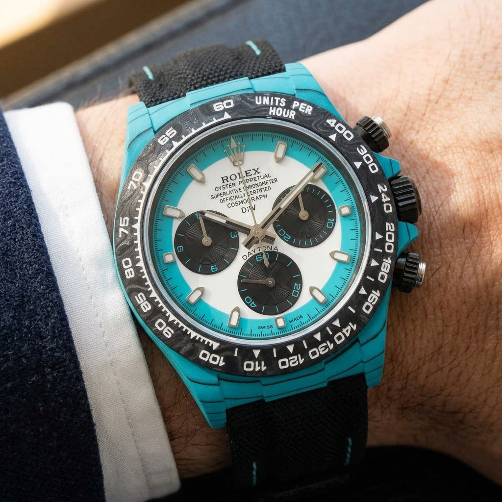 Turquoise-cased chronograph on a black woven strap with turquoise stitching, worn under a cuff