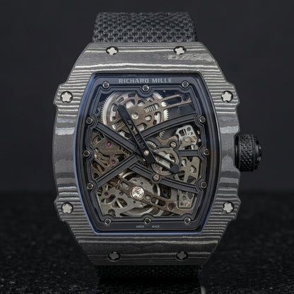 All-black carbon tonneau watch on its black woven strap, worn on the wrist below a dark suit cuff