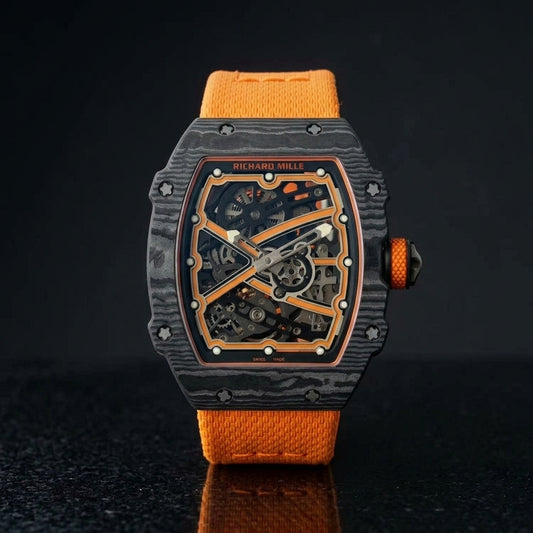 Ultra-thin black carbon tonneau watch with an orange skeleton dial and an orange textile strap, upright on polished black granite
