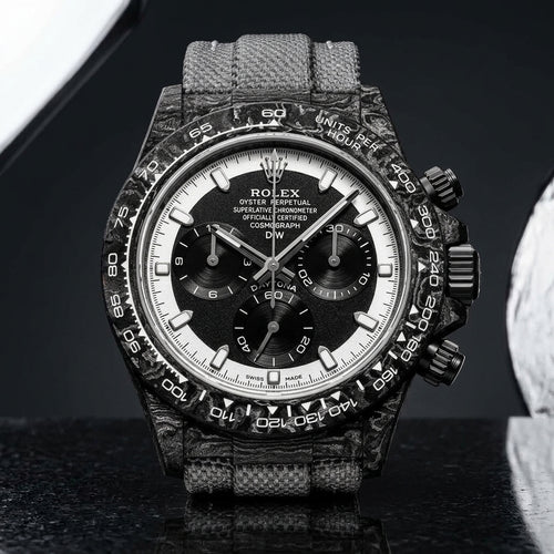 Forged-carbon chronograph with a black dial inside a white chapter ring, on pale stone