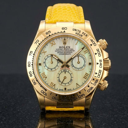 Gold-tone chronograph with a pale yellow mother-of-pearl dial, gold Roman numerals and an engraved tachymeter bezel standing upright on polished black granite
